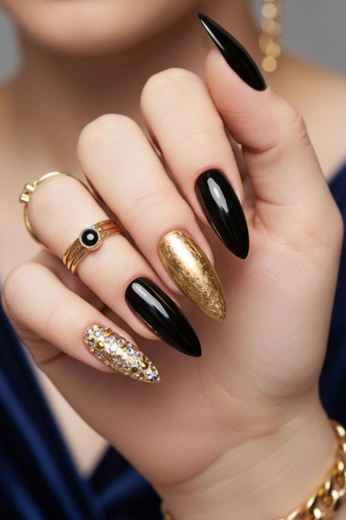 Long black stiletto nails with a metallic gold accent nail and a nail fully covered in gold and clear crystals