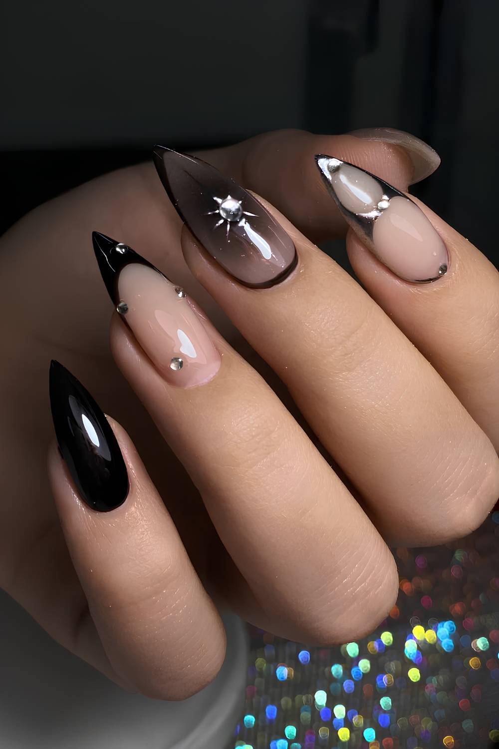 Long stiletto nails mixing solid black glitter, nude nails with black French tips, and a nude-to-black gradient nail with a crystal starburst