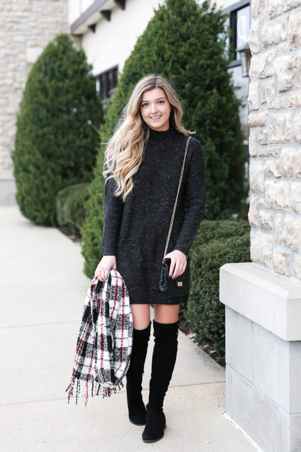 Black sweater dress with a red plaid scarf and over-the-knee boots