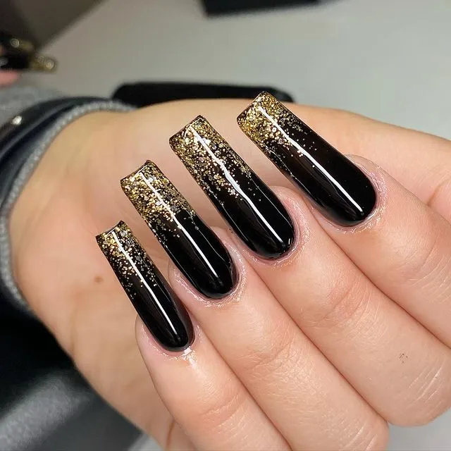 Long square black acrylic nails with gold glitter fading from the tips