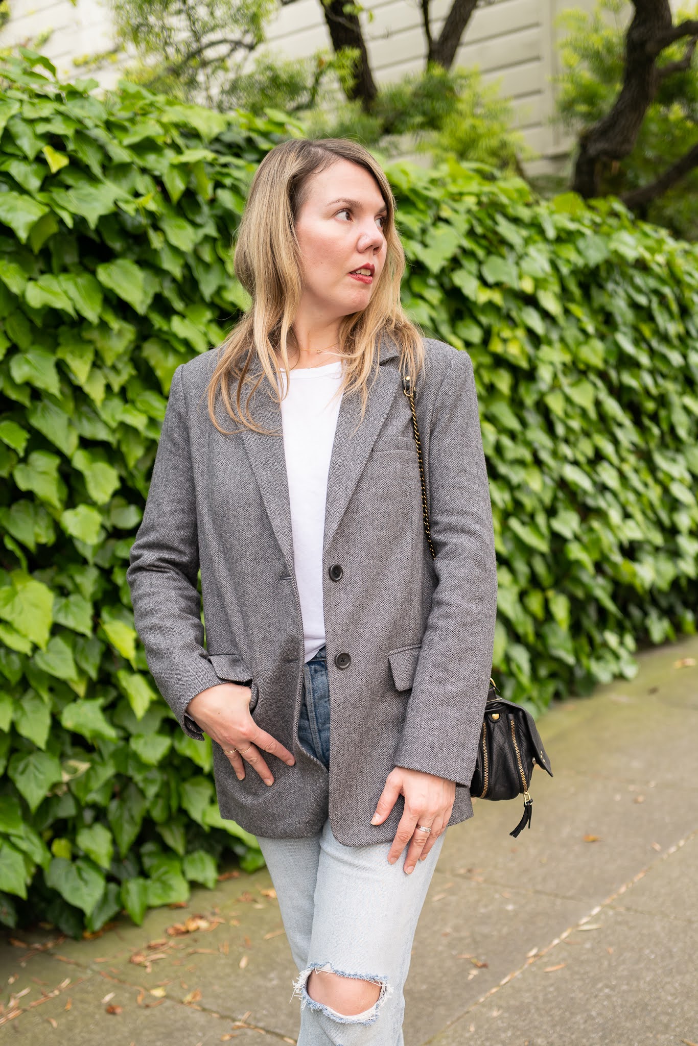 Woman in a grey herringbone blazer with a white tee and ripped light-wash jeans