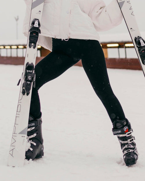 Woman in a white quilted ski jacket and black leggings with ski boots in the snow