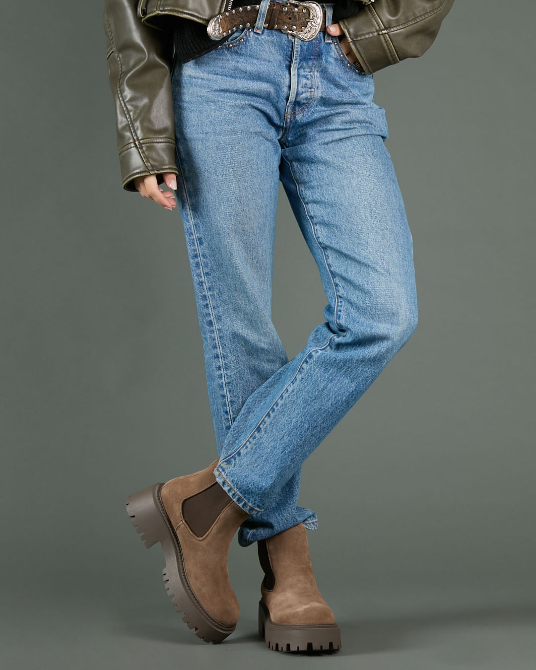 Tan suede chelsea boots worn with blue jeans, olive leather jacket and western buckle belt