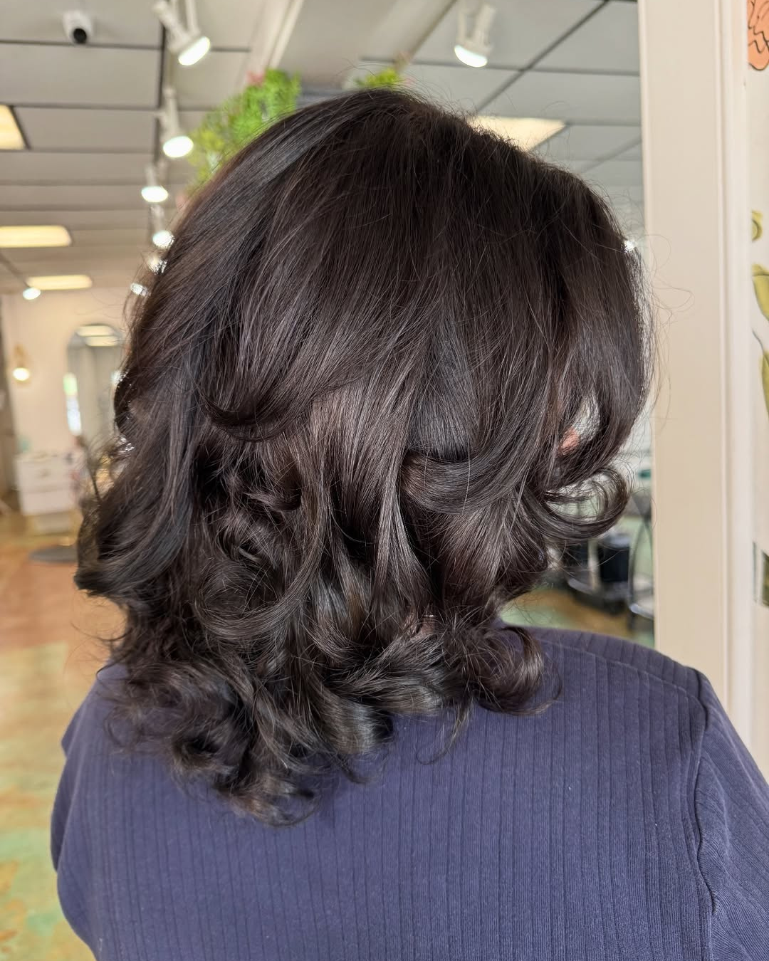 Voluminous bouncy blowout with curls on medium-length dark hair, salon back view