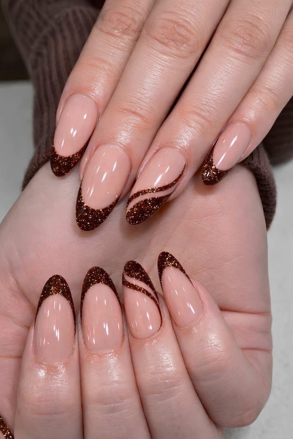 Almond nails with nude base and copper glitter French tips with swirl accent
