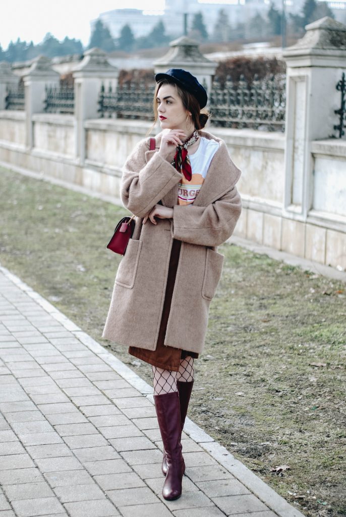 Camel coat over a graphic tee, printed scarf, suede midi skirt, fishnet tights and burgundy knee-high boots