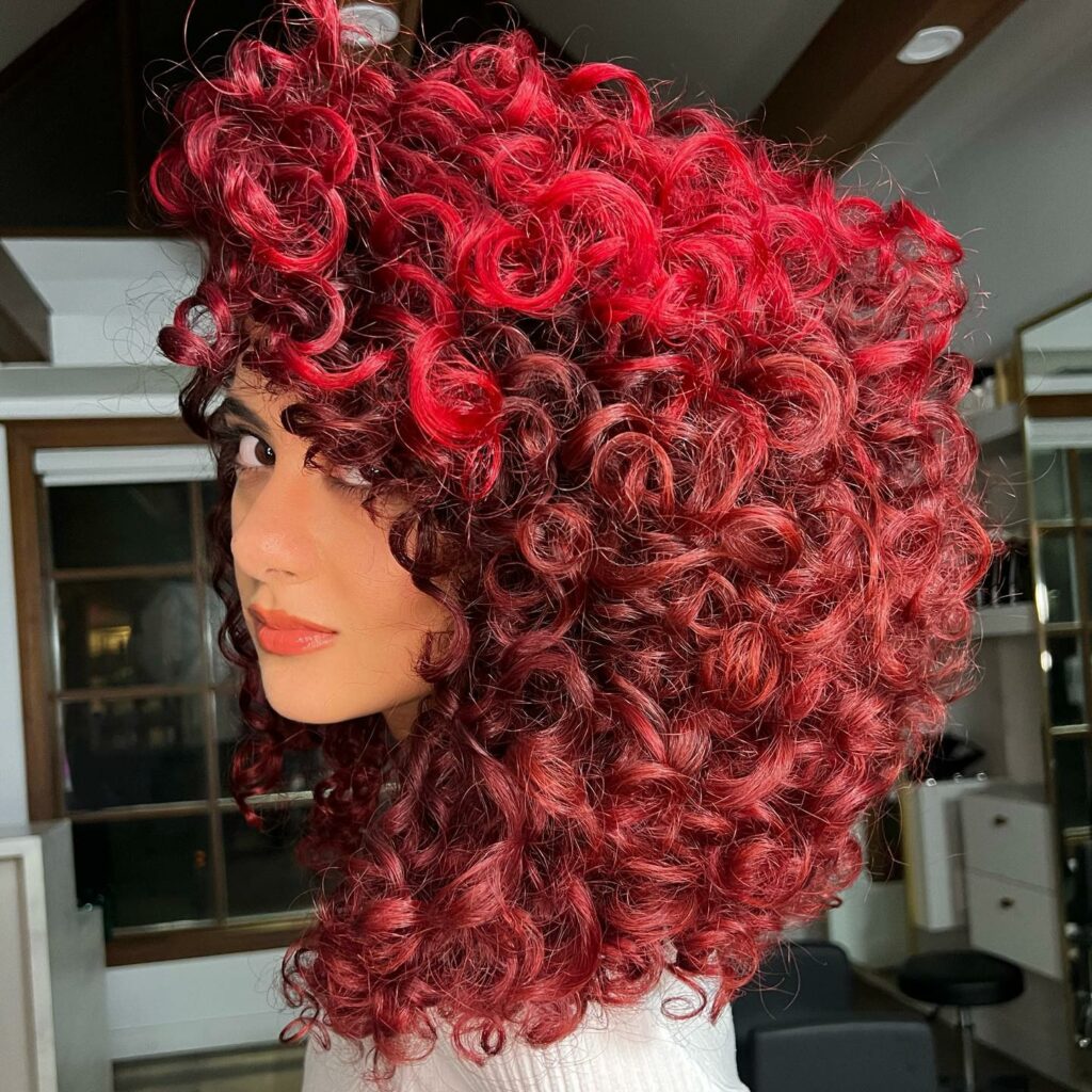 Voluminous vivid scarlet red curls, side view in a salon