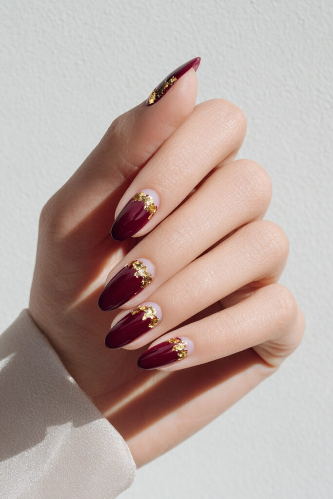 Burgundy almond nails with gold foil near the cuticles