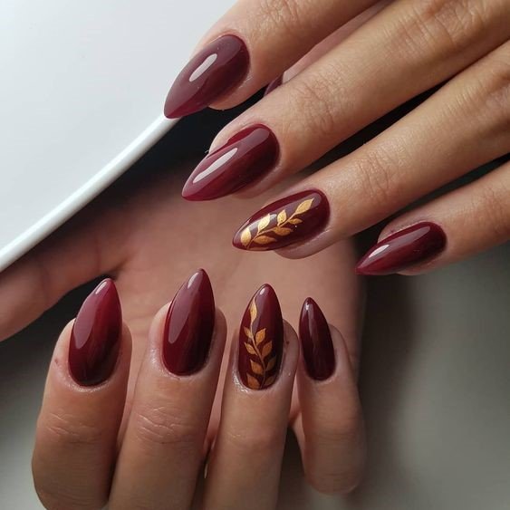 Glossy burgundy almond nails with gold laurel leaf accent art