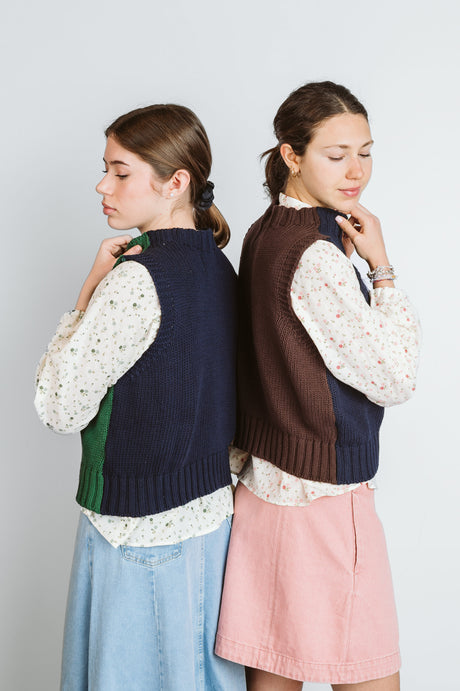 Two models wearing color-block knit vests layered over floral blouses with skirts