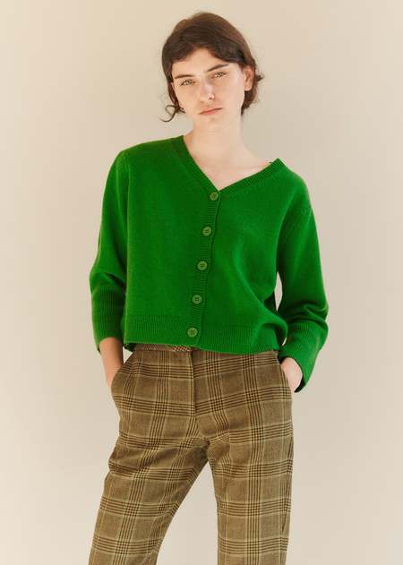 Woman wearing a forest green buttoned cardigan with brown plaid trousers