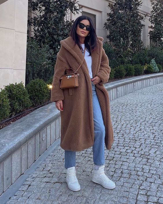 Woman in a camel teddy coat, white t-shirt, light-wash jeans and white sneakers