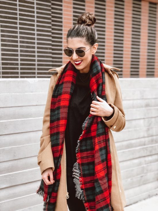 Woman in a camel coat with a red plaid scarf over a black top
