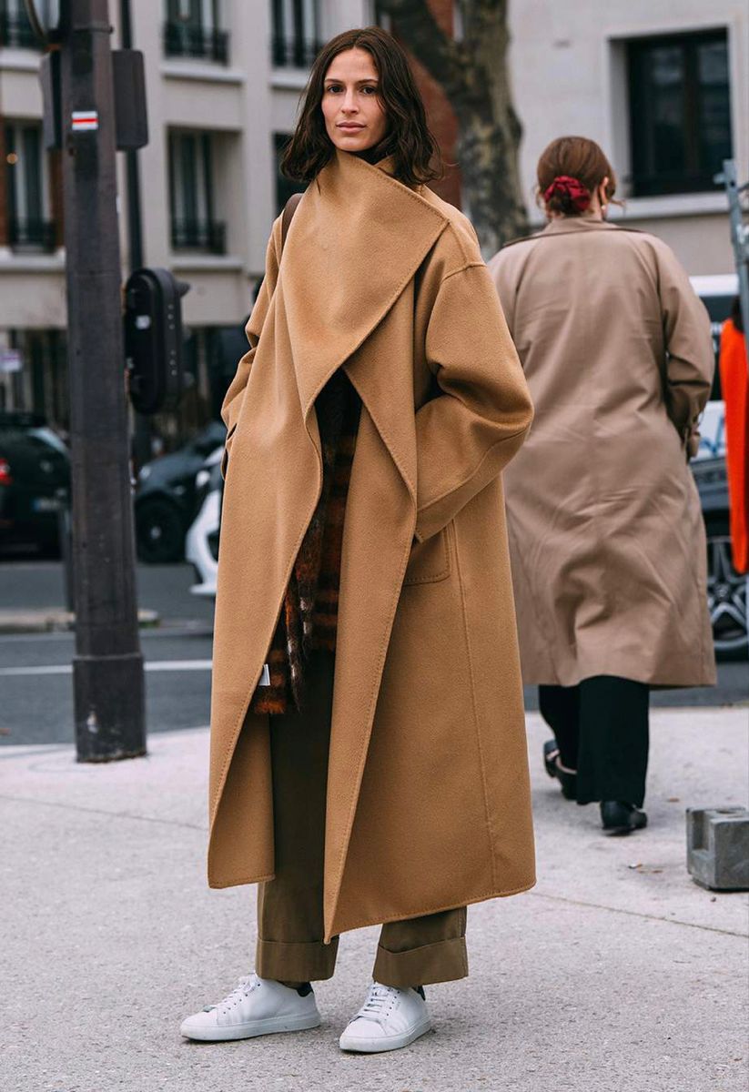 Woman in a camel wrap coat with a plaid scarf, olive trousers and white sneakers