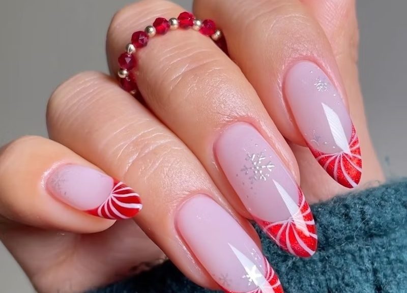 Peppermint candy-swirl French tips on oval nails with small silver snowflakes