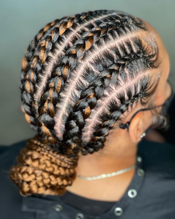 Black feed-in braids with caramel streaks gathered into a braided bun