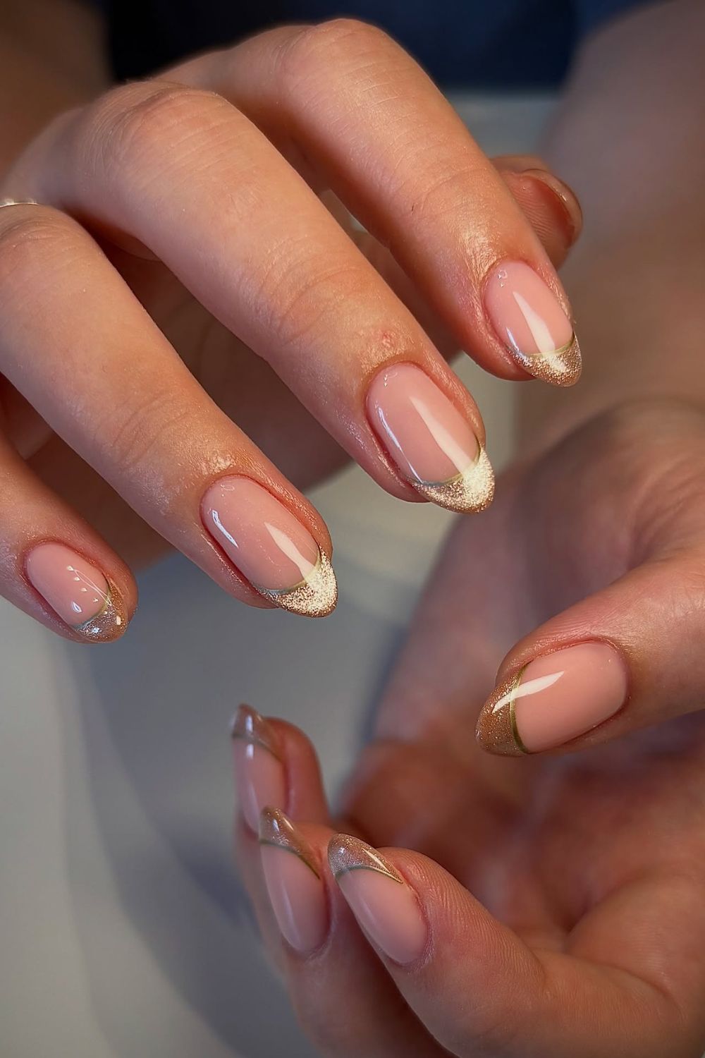 Almond nails with a nude-pink base and champagne-gold glitter French tips; real photography.