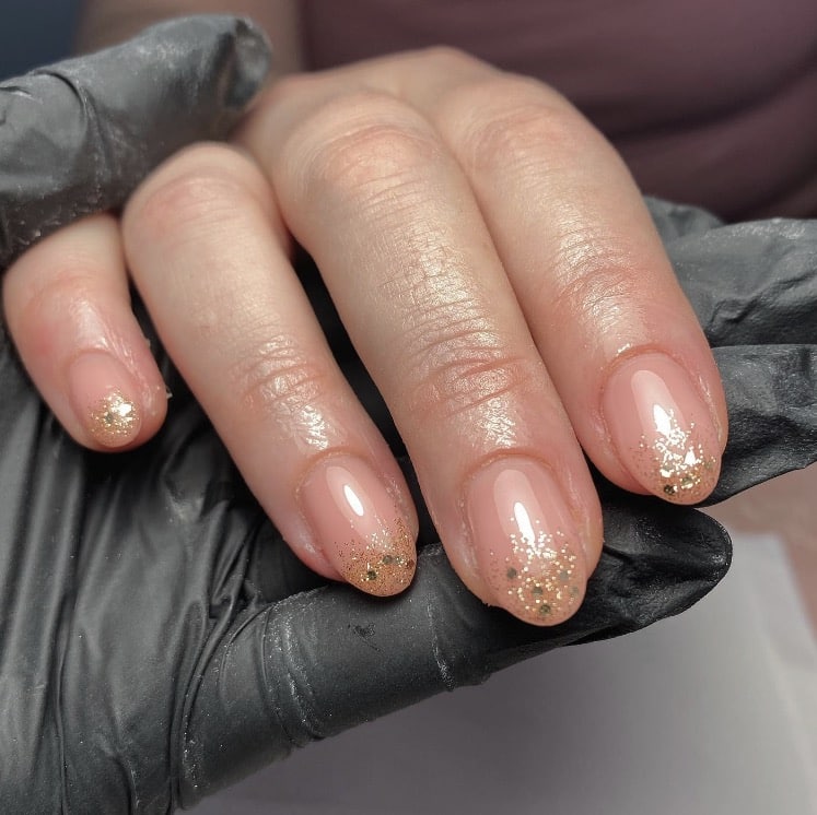 Short almond nails with nude base and champagne glitter accents
