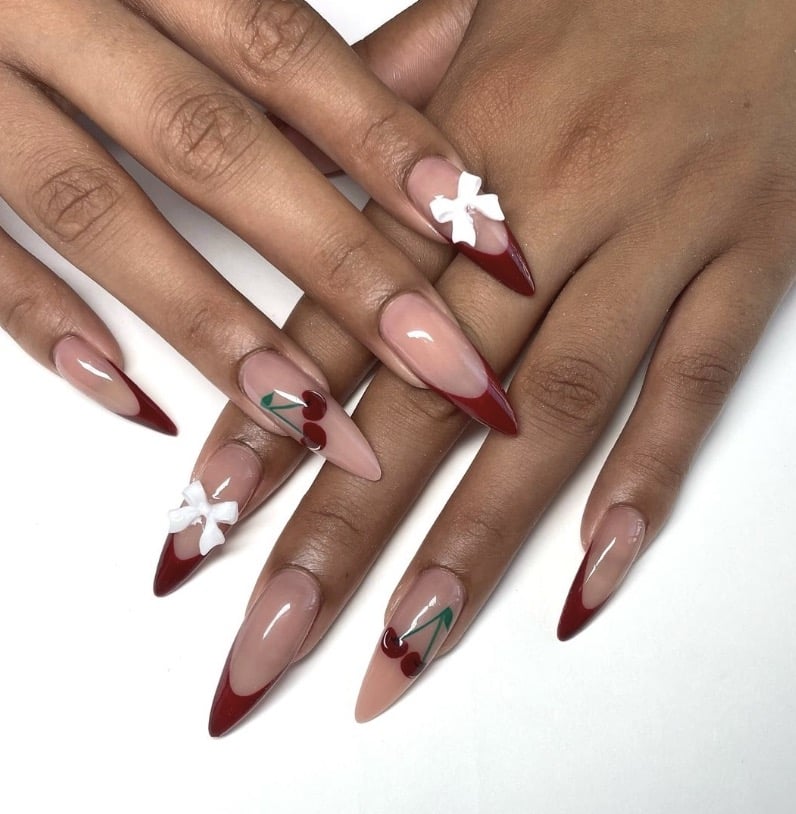 Nude stiletto nails with deep red french tips, cherry nail art and white bow charms