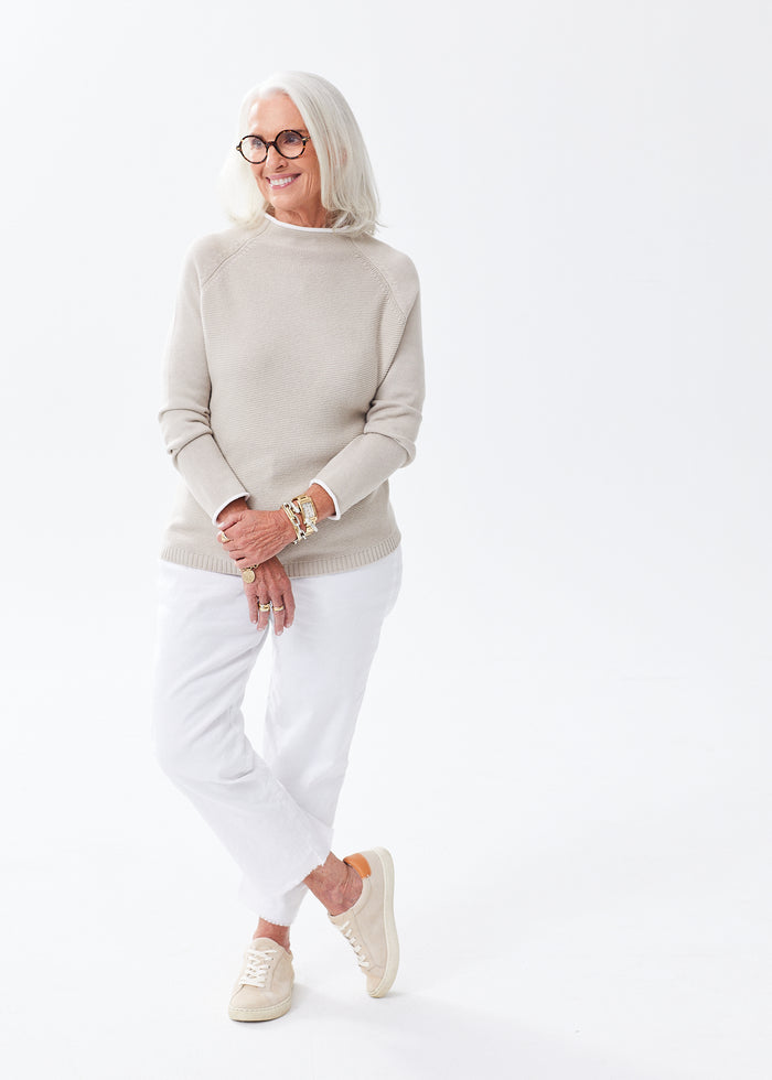 Senior woman in an oatmeal chunky knit sweater with white jeans and tan boots