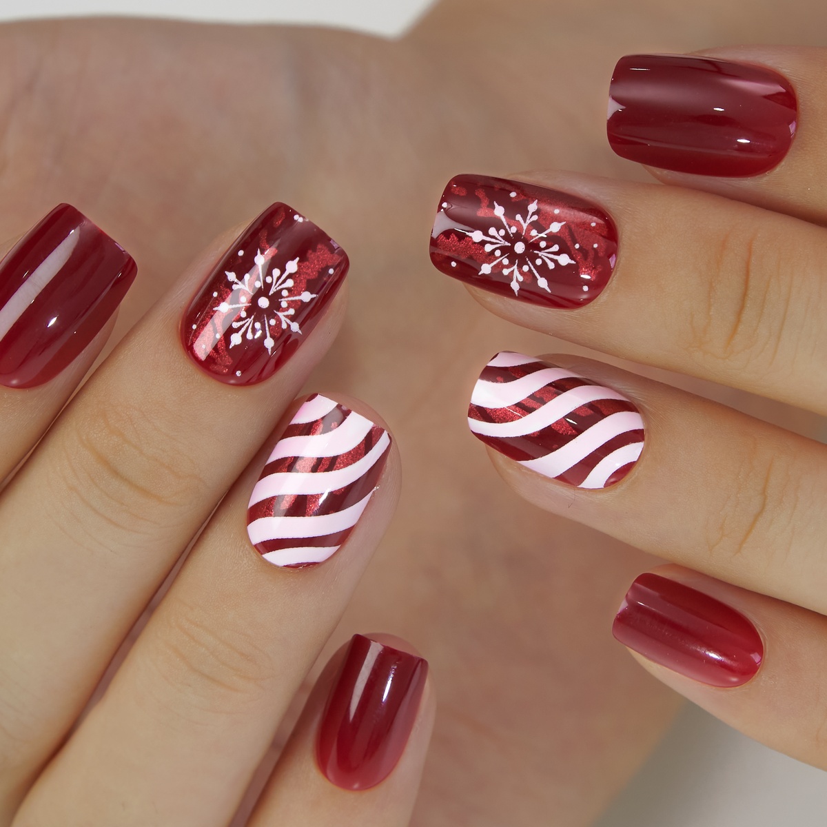Short squoval nails in glossy wine red with diagonal candy-cane stripe and snowflake accent nails