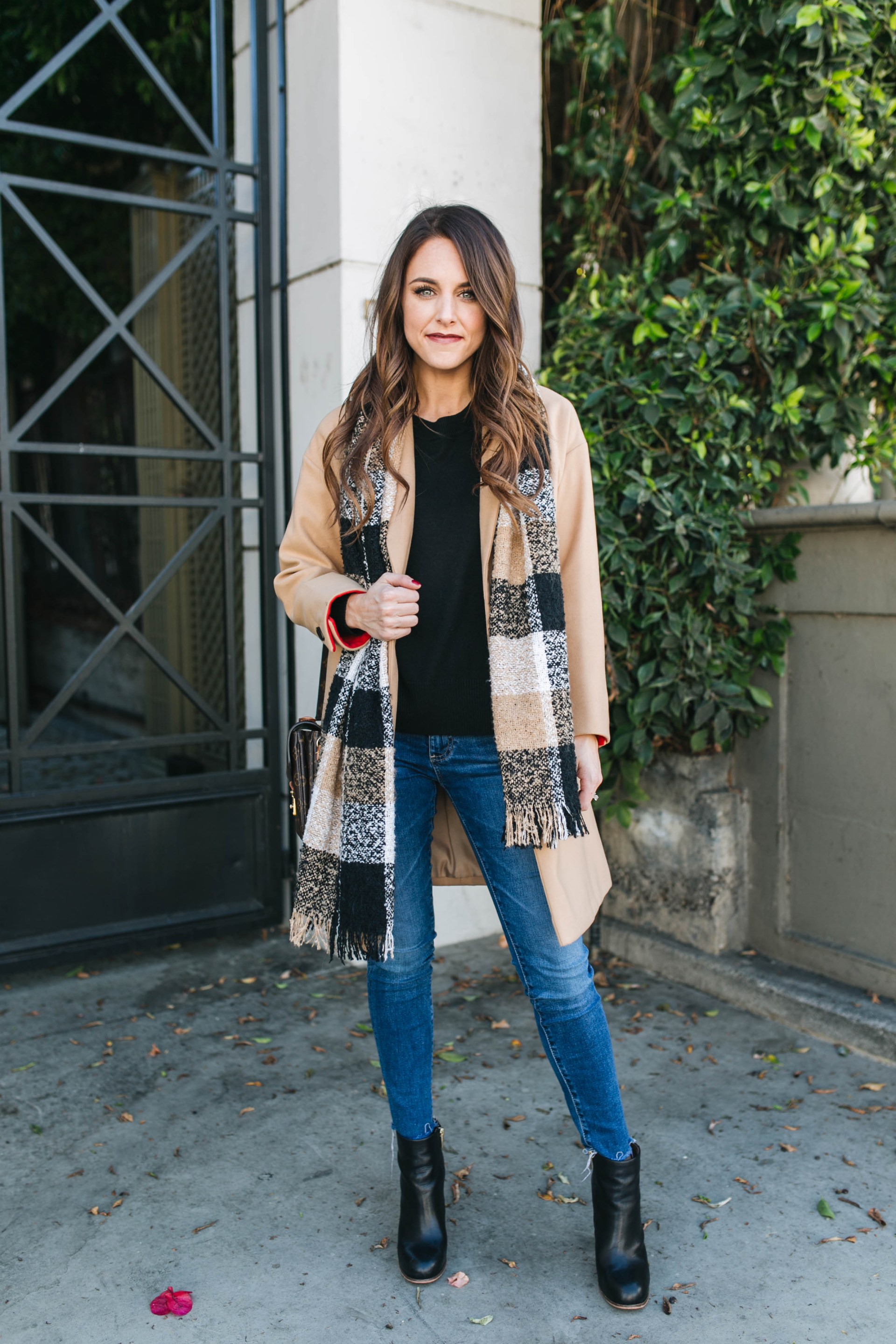 Woman in a camel coat with a plaid scarf, blue jeans and black ankle boots