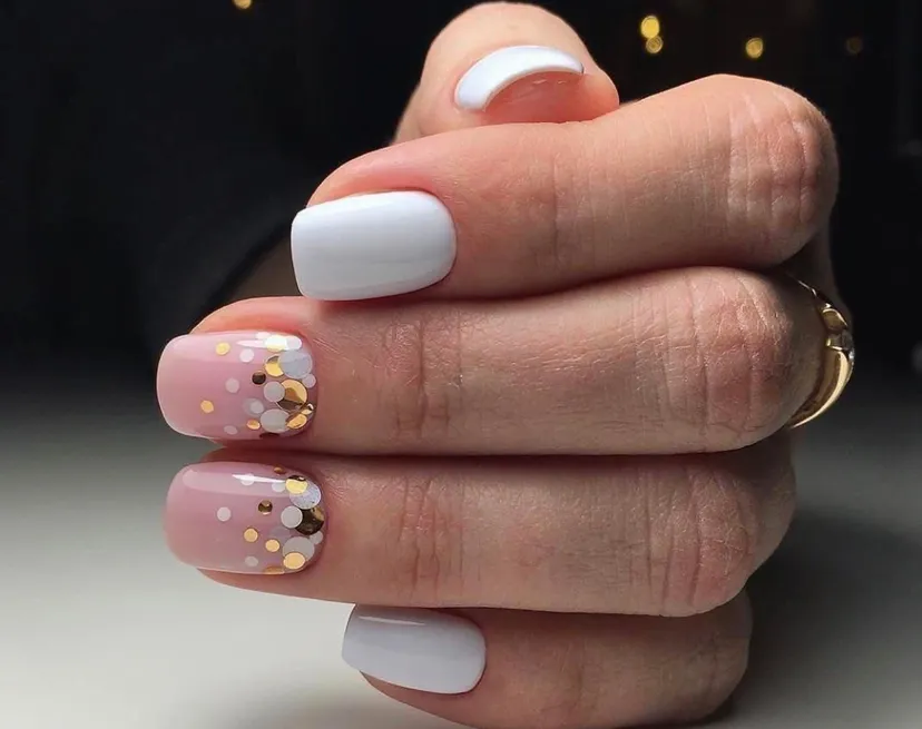 Short square nails with gold silver and white confetti dots over a sheer nude base, alternating with solid white nails