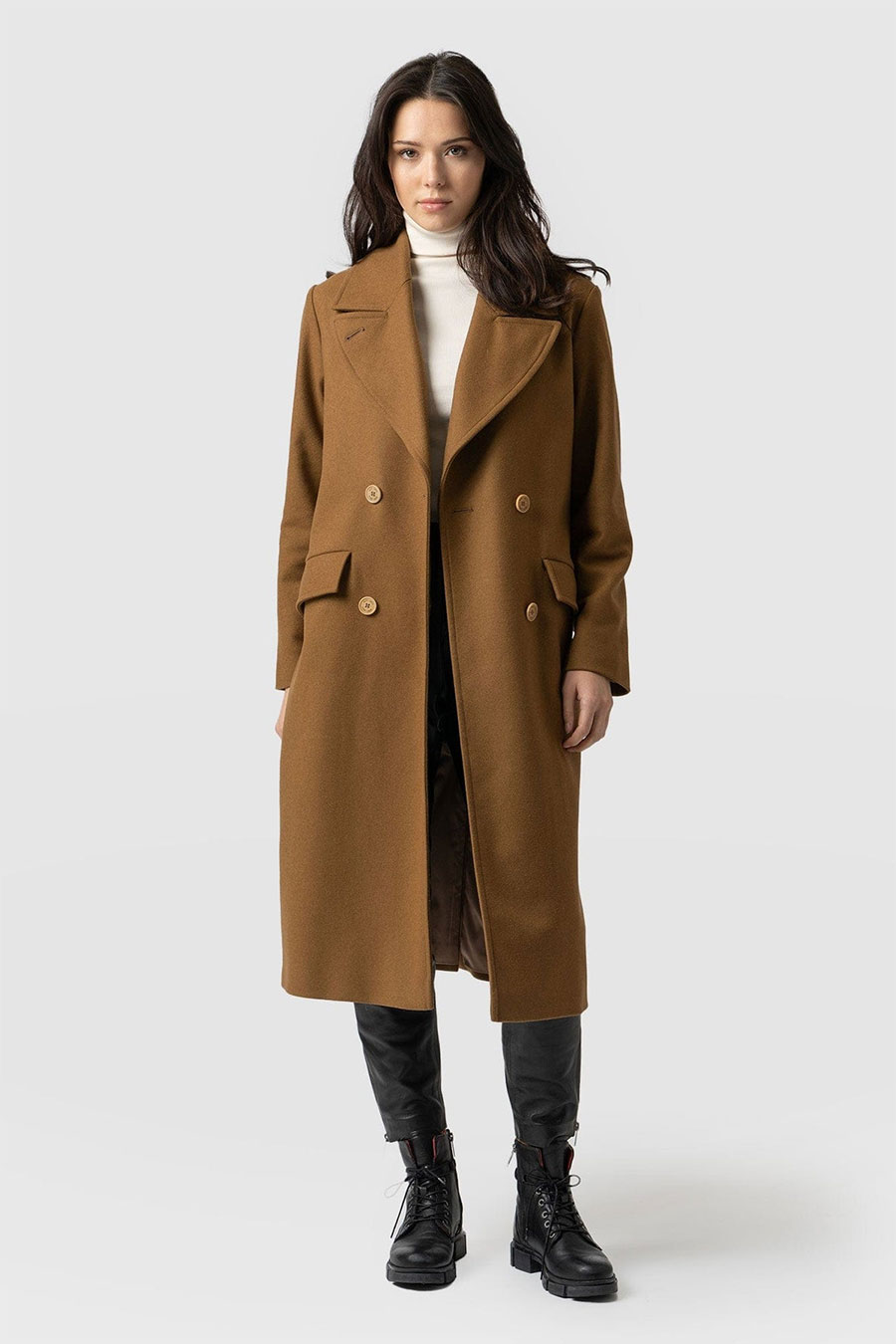 Double-breasted camel-brown wool coat over a white turtleneck with black leather pants and combat boots