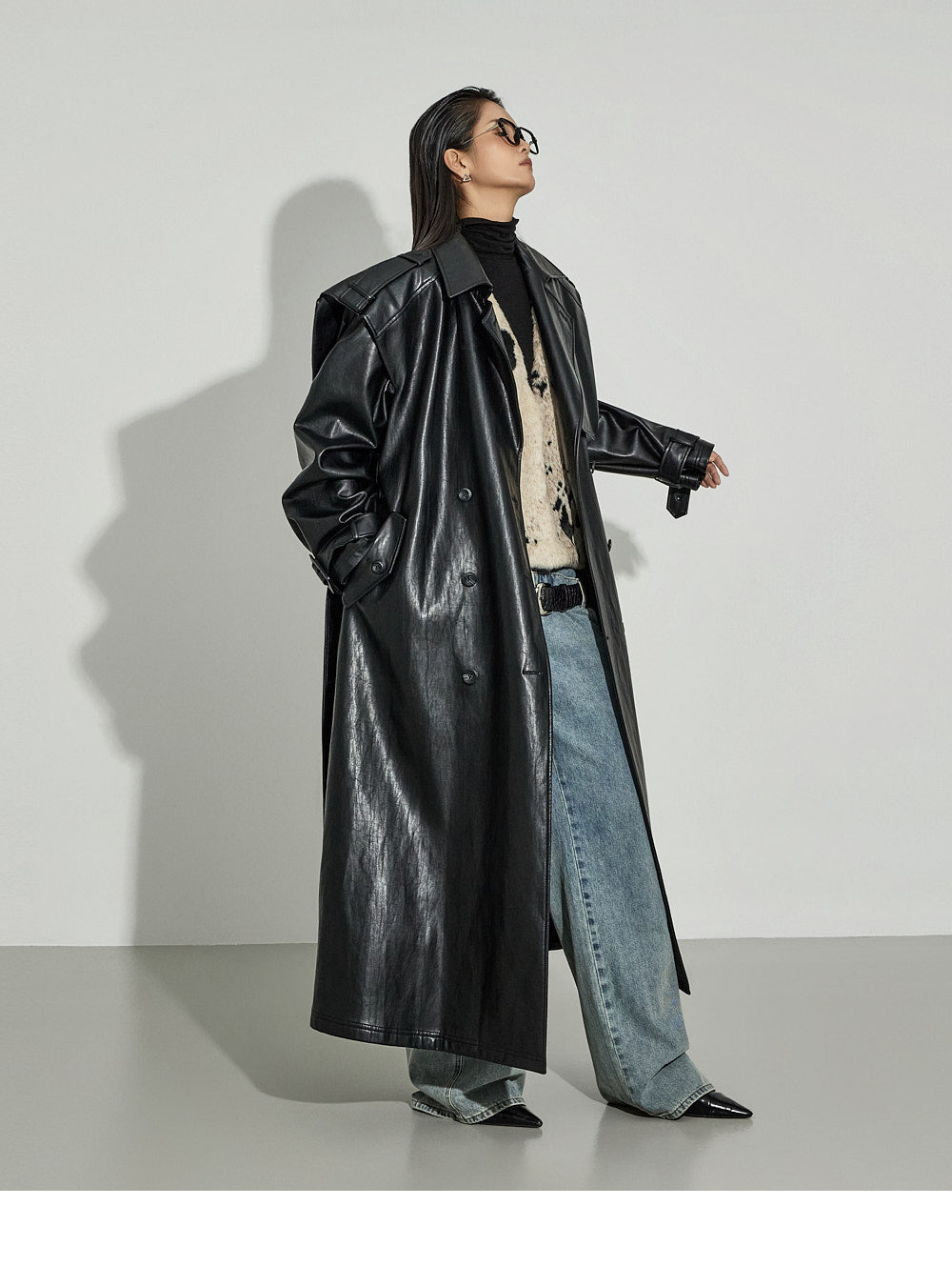 Black faux leather trench coat over fuzzy patterned sweater with light-wash wide-leg jeans