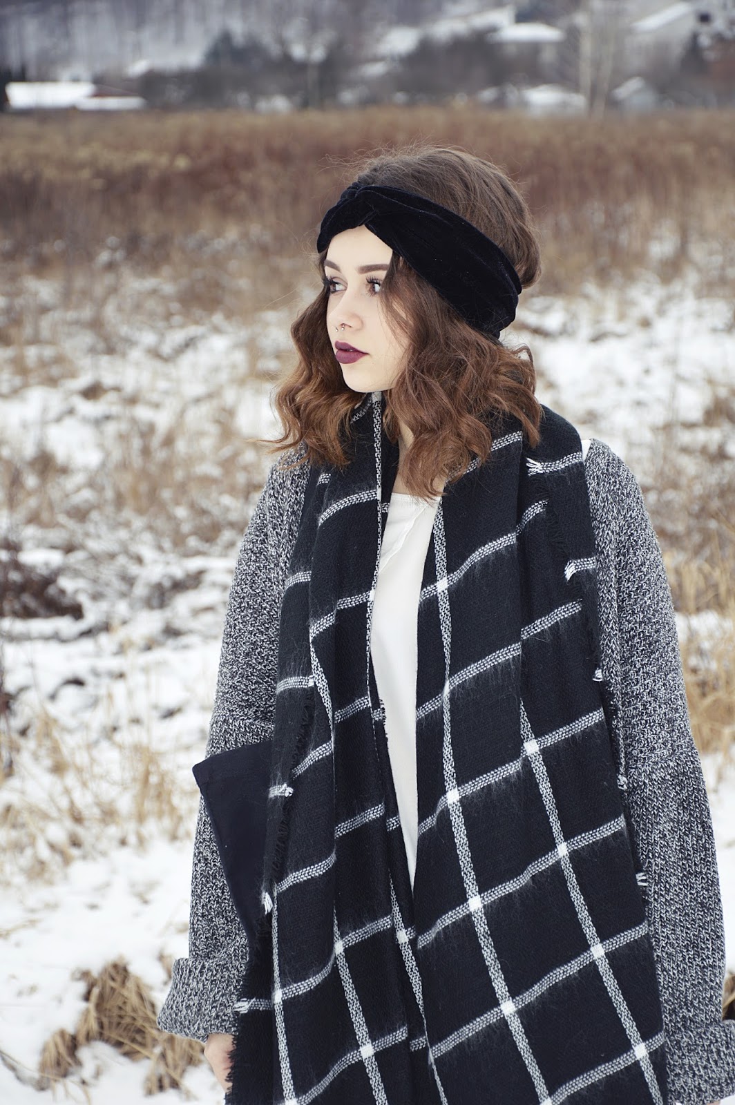 Woman in a snowy field wearing a black twisted velvet headband and a black and white check blanket scarf