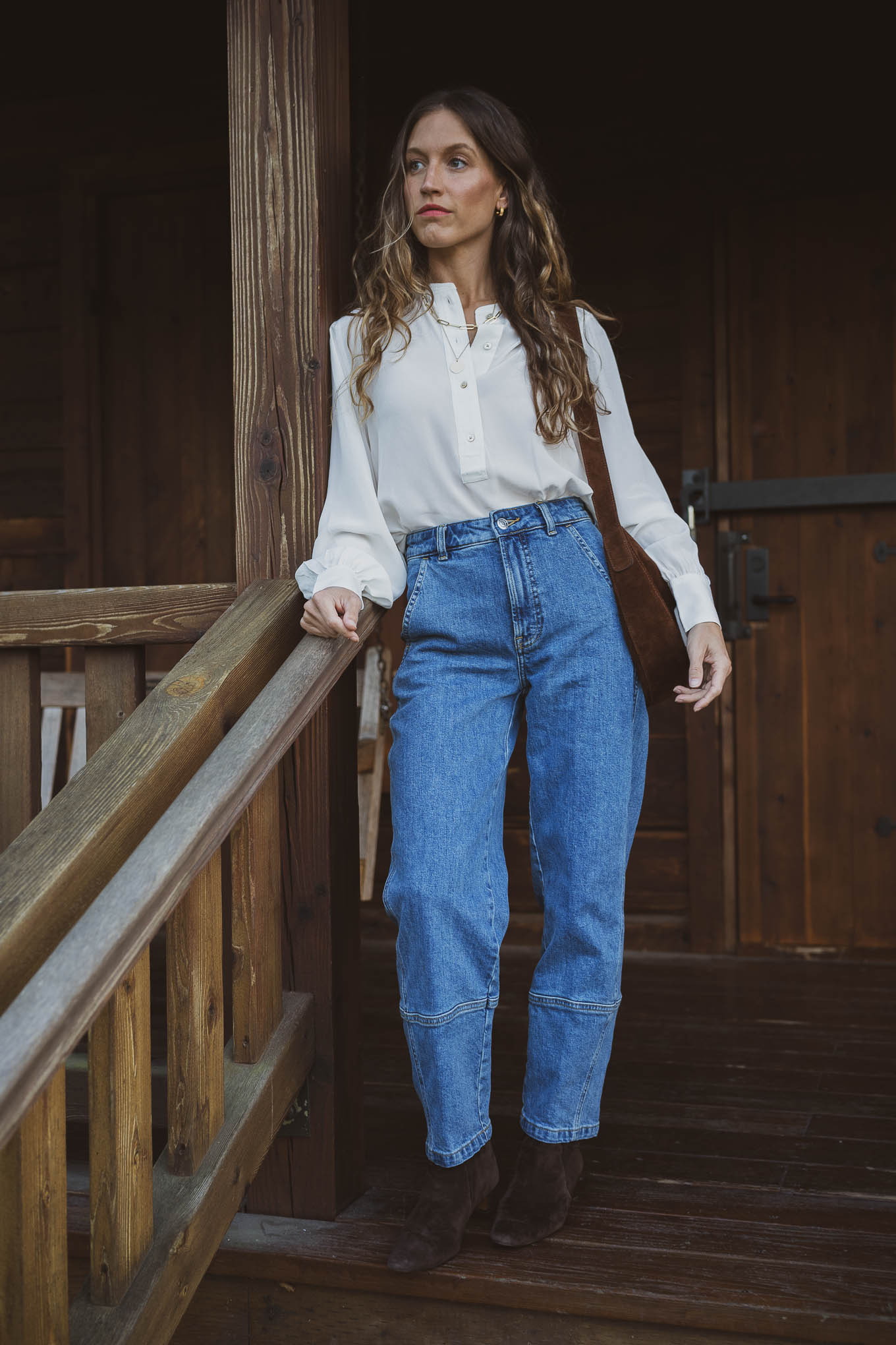Woman wearing dark brown suede ankle boots with a white blouse and blue barrel-leg jeans