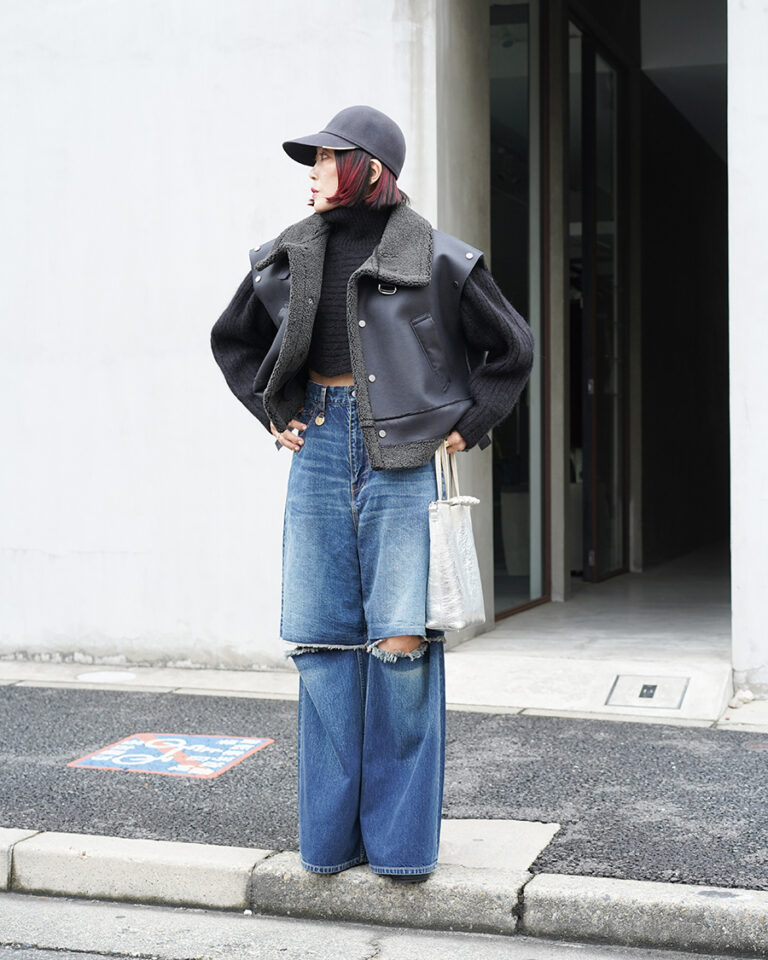 Street style: black leather vest with shearling collar, black cropped knit, ripped wide-leg jeans, silver tote and cap