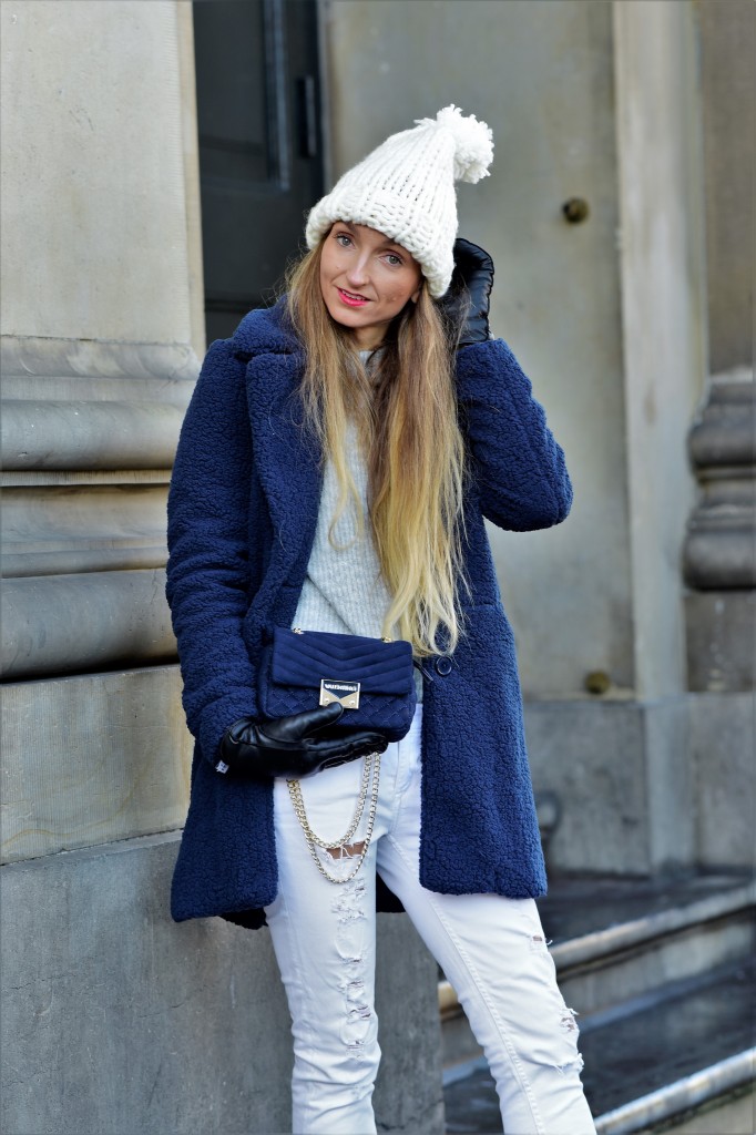 Woman in a navy teddy coat with white ripped jeans and a pom beanie