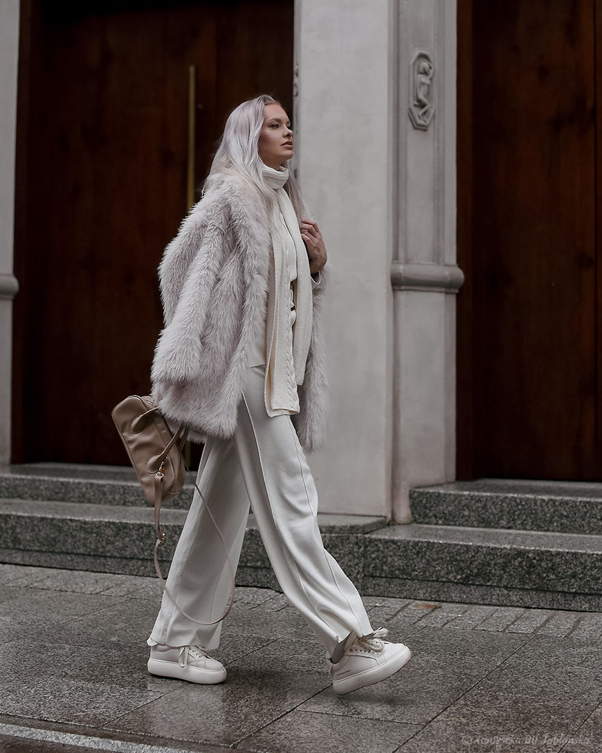 Woman in an all-white outfit with a cream faux-fur coat, wide white trousers and chunky white sneakers