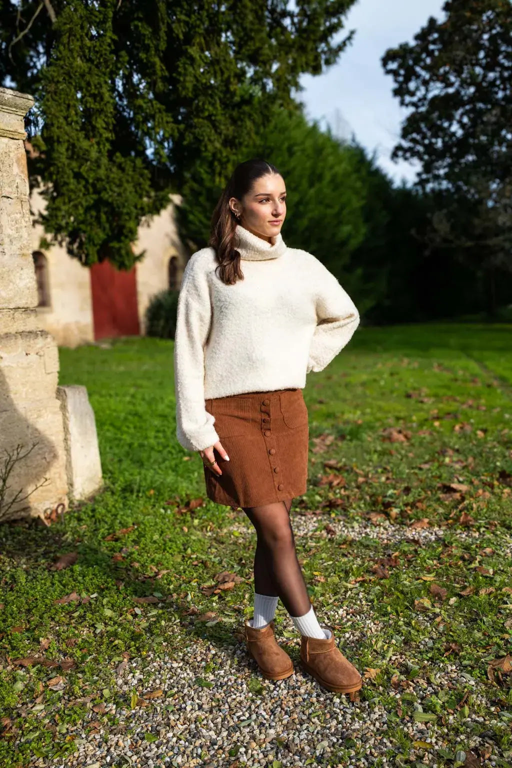 Woman wearing a camel corduroy button-front mini skirt, cream fuzzy turtleneck, black tights and tan shearling boots