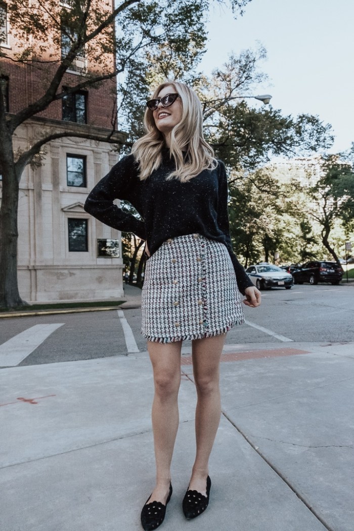 Woman wearing a black knit sweater with a houndstooth tweed mini skirt and black studded loafers