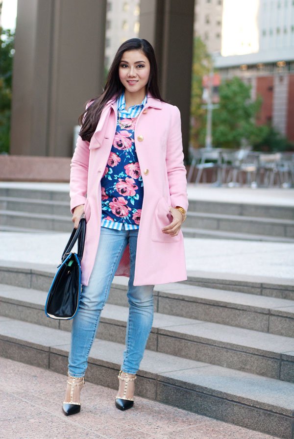 Woman in a pink short wool coat with a floral print dress over skinny jeans and studded heels