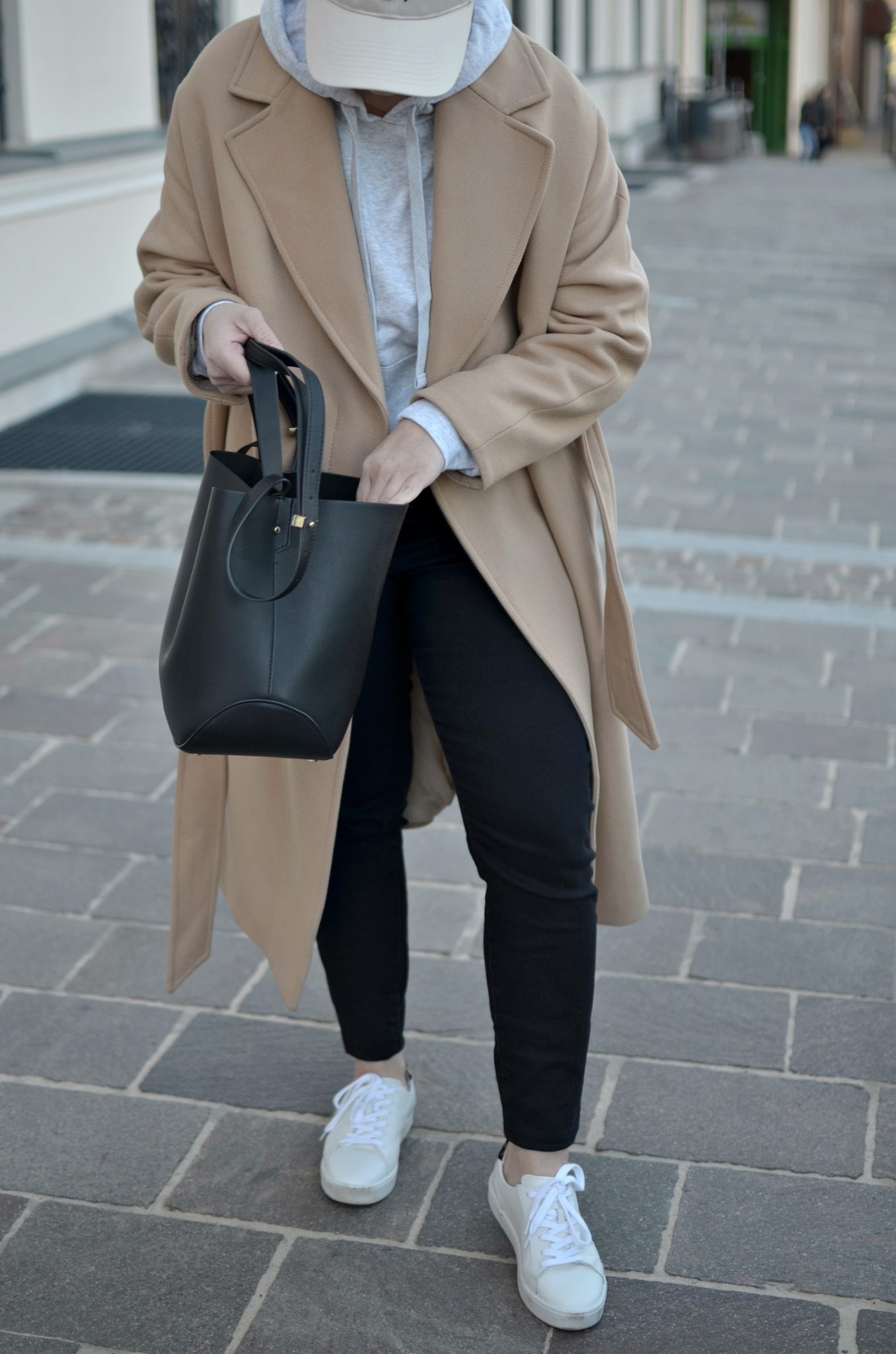 Woman in an oversized camel coat with a grey hoodie, black joggers and white sneakers