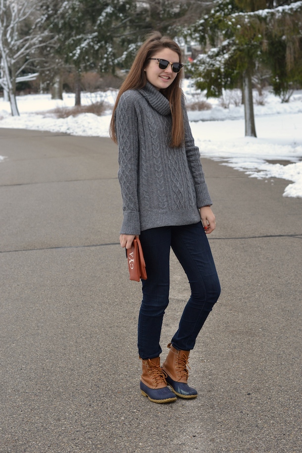 Woman wearing a grey cable-knit turtleneck with dark jeans and tan duck boots