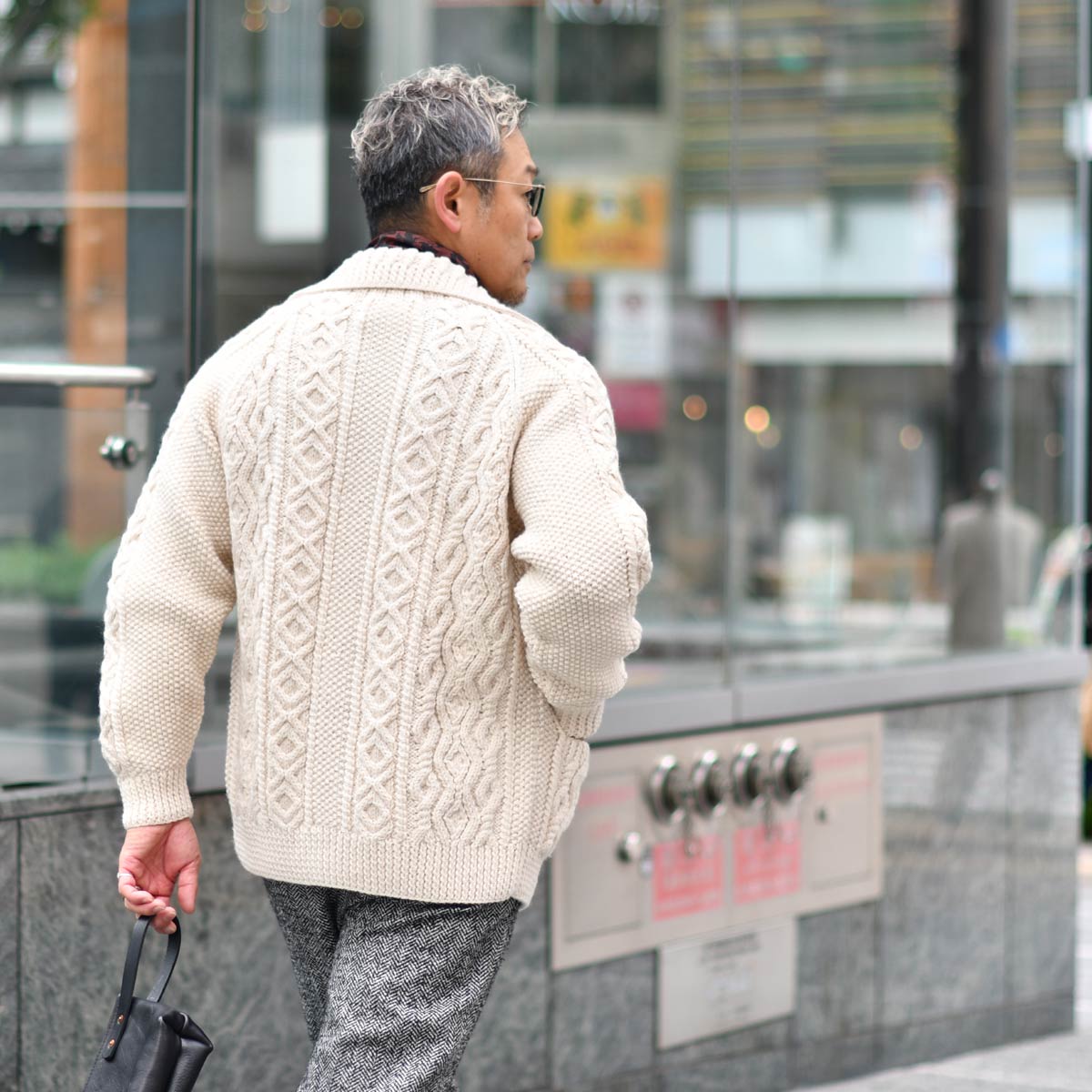 Chunky cream fisherman-knit cardigan with gray tweed trousers, shown on a men's frame for texture reference