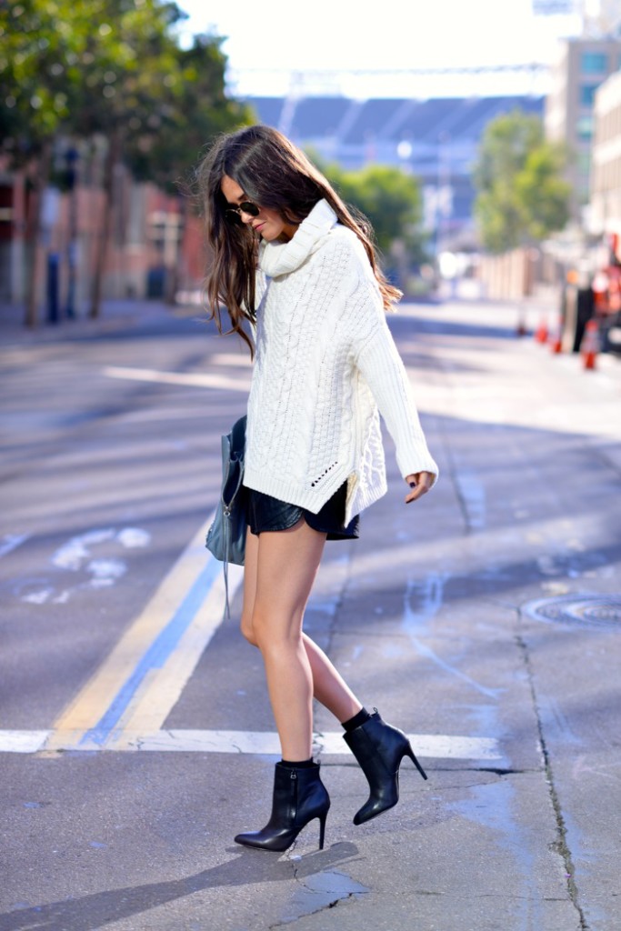Woman in an oversized white cable-knit turtleneck, black leather mini skirt and black stiletto ankle boots