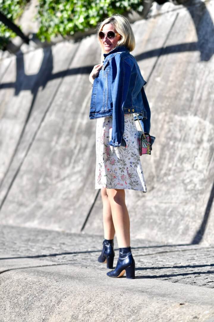 Woman in a floral tea dress, denim jacket and black heeled ankle boots