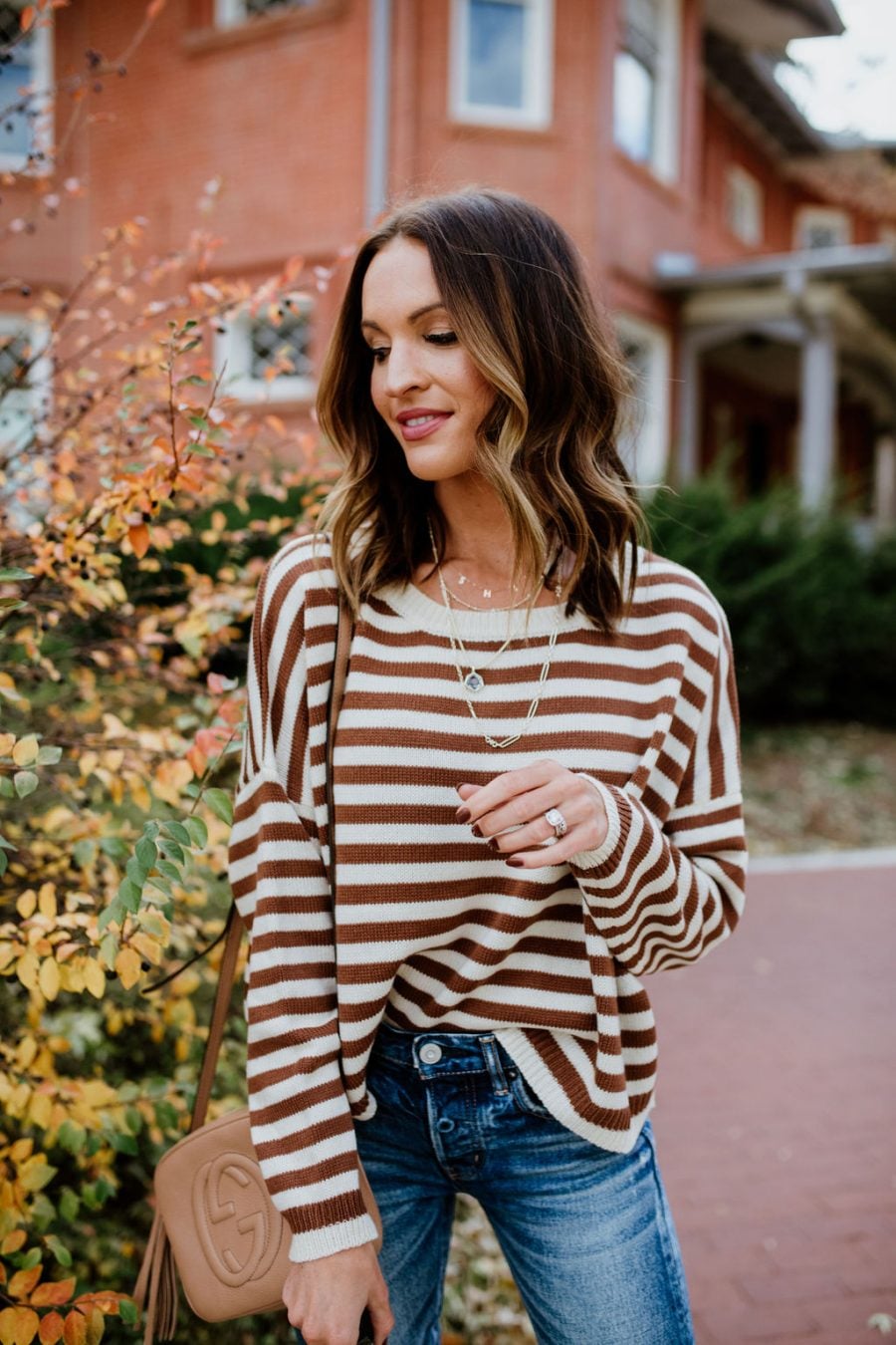 Woman wearing a brown-and-cream striped crewneck sweater with dark-wash jeans and layered necklaces