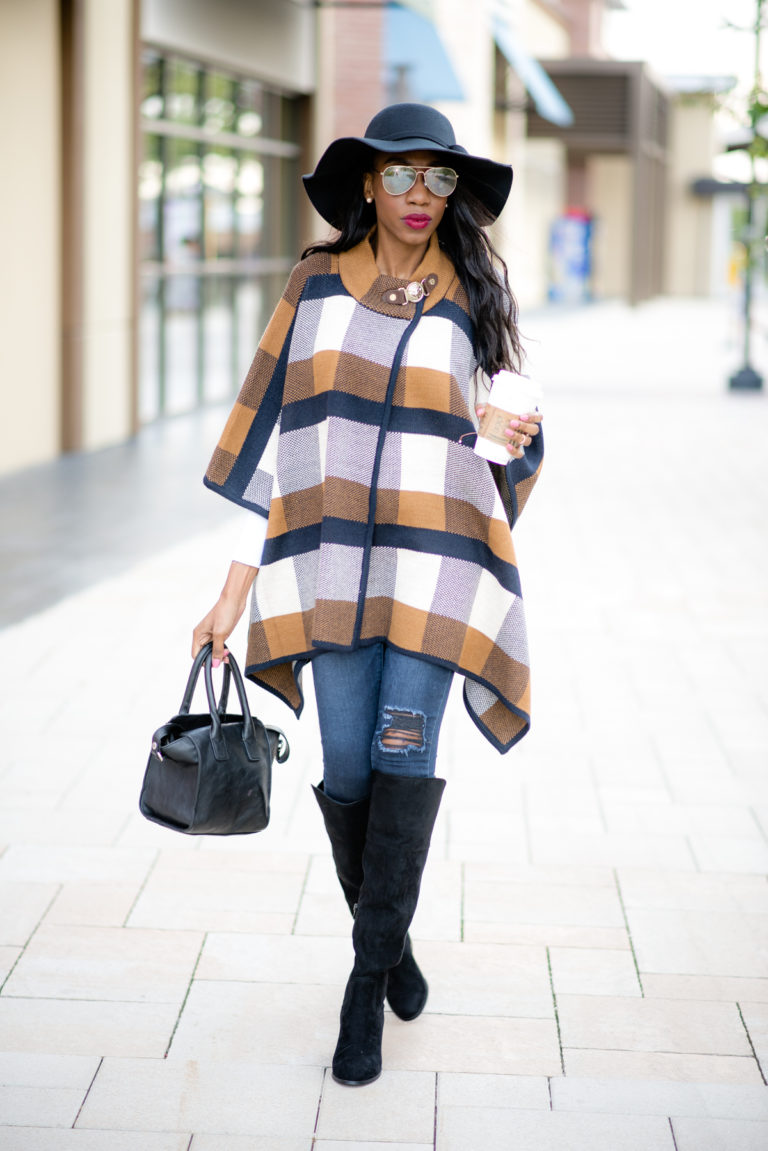 Woman in a mustard navy and cream check poncho, black floppy hat, ripped jeans and black over-the-knee boots