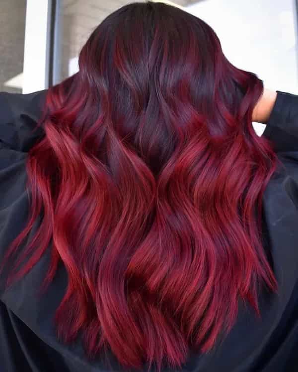 Back view of long wavy hair with dark roots melting into vivid dark-red balayage