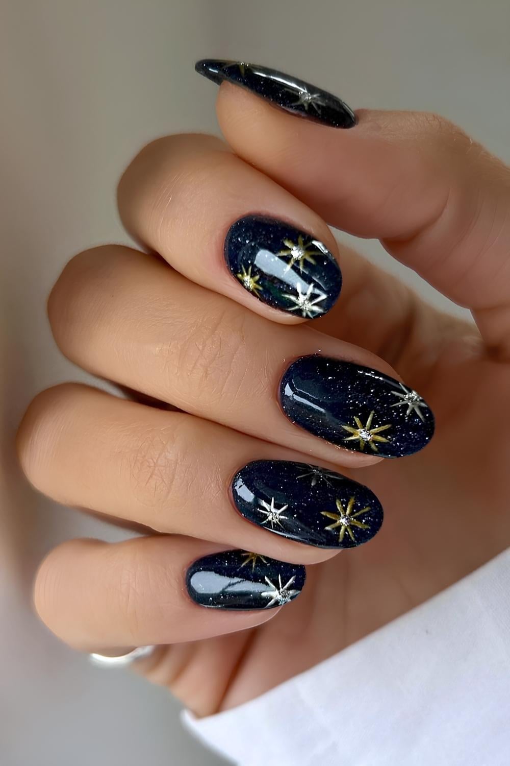 Oval nails in deep navy glitter polish with gold and silver starburst nail art