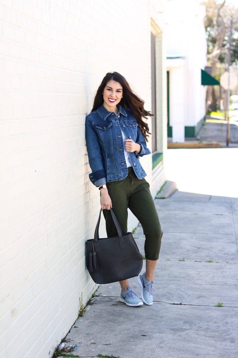 Woman in a classic denim jacket, white tee, olive jogger pants, gray sneakers and a black tote bag