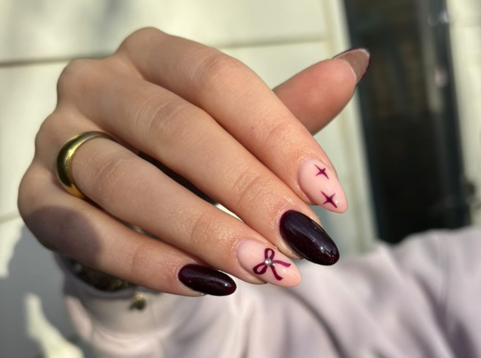 Medium almond nails in dark cherry with hand-painted pink bows on accent nails