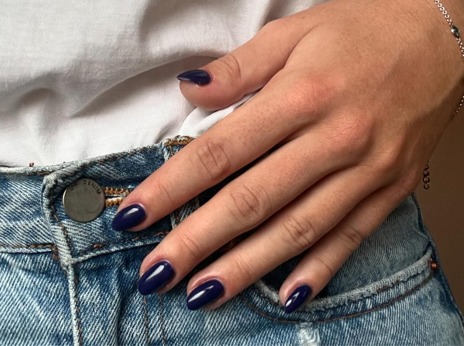 Medium almond nails in deep glossy indigo blue, hand on denim