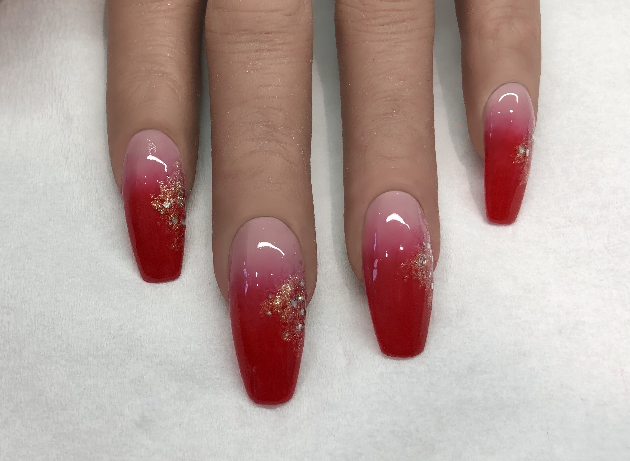 Long coffin nails fading from nude to red with gold glitter dusted along the sides